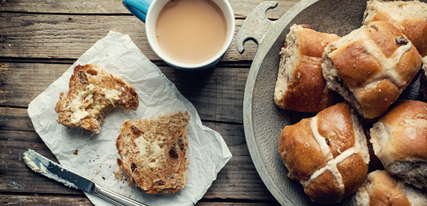 a stack of hot cross buns with butter and a cup of tea